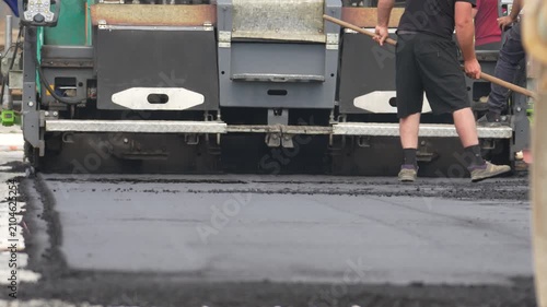 Road roller compacts hot asphalt on the road. Worker focuses on guiding the machine. Black pavement spreads smoothly. Construction workers work hard. Ideal for road-building projects