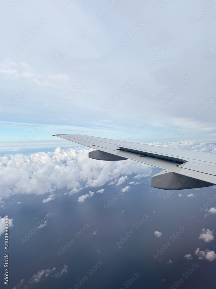 Fototapeta premium Scenic passenger view from an airplane window looking over the aircraft wing in flight. Beautiful white cumulus clouds spread below and across a blue sky daytime horizon.