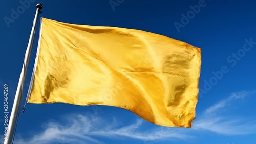 A bright yellow flag ripples in the wind against a clear blue sky
