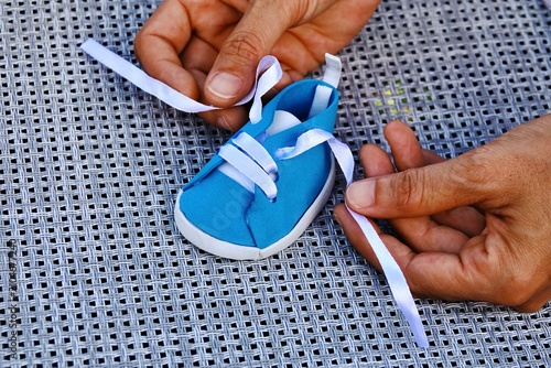 Tableau sur toile Hands tying the laces on a small blue baby sneaker on a textured surface