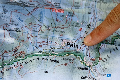 Hand pointing to a topographic map of Stelvio National Park in the Italian Alps. A person's hand indicates a specific location on a detailed topographical map of the mountainous Stelvio National Park 