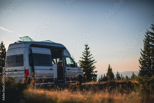 Camper van parked in a peaceful forest clearing during golden hour, showcasing van life and outdoor travel