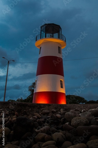 Lighthouse at night, illuminated red, rocky shore, serene atmosphere High quality commercial imagery suitable for marketing, advertising, editorial us