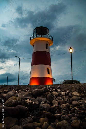 Puntarenas, Costa Rica, Lighthouse on stones, red and white striped, cloudy sky, rocks, natural beauty, serene, peaceful, calm, tranquil, outdoor lifestyle, adventure, exploration, travel, destination