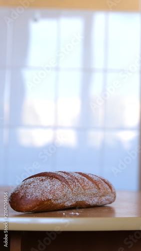 An oval loaf of fresh rye or wheat bread with oblique cuts, sprinkled with flour, on the table.