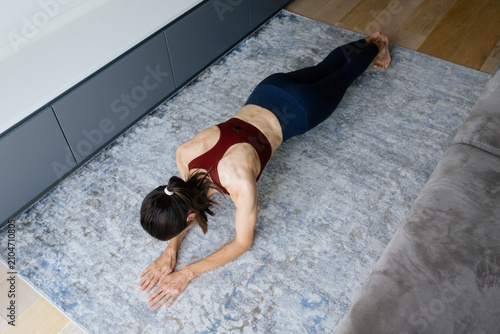 Fit woman performing a plank exercise on a rug at home, focusing on core strength, fitness, and a healthy lifestyle