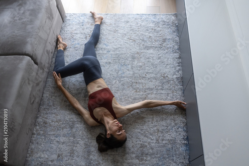 Fotografía Woman performing a supine spinal twist, stretching her body on a rug by a sofa,