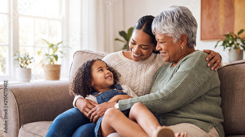 A grandmother, mother, and daughter smiling and bonding while sitting together on a comfortable sofa in a bright, modern living room.