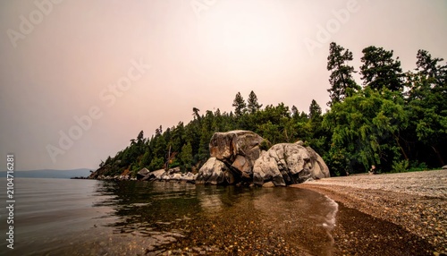 Rocky lake shore with pine trees under twilight sky.