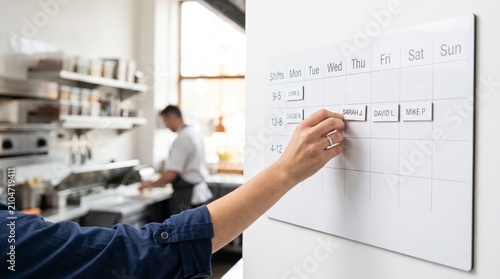 Restaurant manager organizing staff work shift schedule on whiteboard