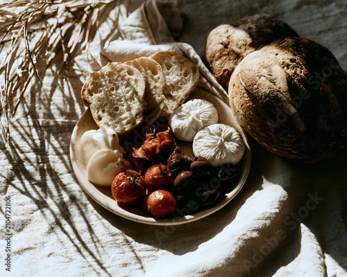 Artisan charcuterie board with bread, cheese, olives, and tomatoes, styled with dried palm leaves and natural linen fabric