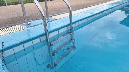 Stainless steel swimming pool ladder at blue tiled edge