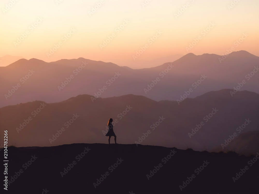 Fototapeta premium Silhouette of a woman standing on a mountain ridge at sunset