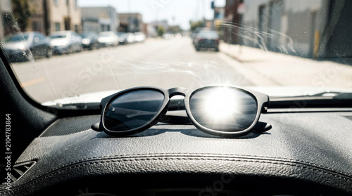 Stylish black sunglasses on a vehicle dashboard with bright sun flare and a blurry street background