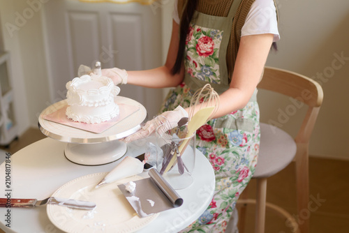 Fotografie Asian woman whisking batter while decorating homemade white cake in bright home