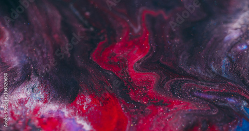 Shimmering acrylic. Art fluid blur. Red paint wavy lava stream swirling in black sparkling liquid on abstract color flare background.