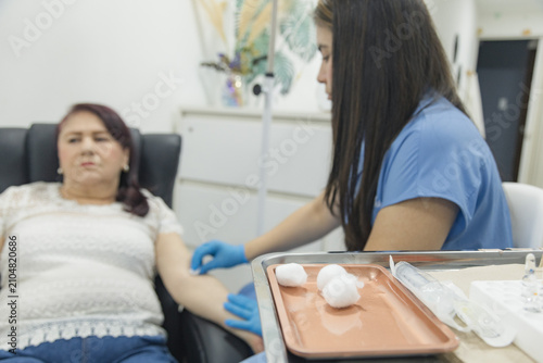 Bild auf Leinwand Medical professional wearing protective gloves prepares a patient's arm for intravenous treatment while sterile medical supplies remain ready on a treatment tray in a healthcare clinic