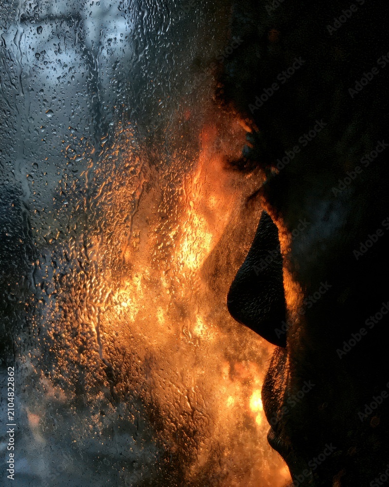 Obraz premium Silhouette shows rain droplets outside the window. Firelight creates warmth inside, highlighting contrast and resilience against struggles.
