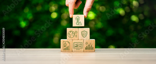 Climate risk management concept with hand placing heat warning icon cube on wooden pyramid blocks showing global warming impact urban safety environmental protection and sustainability planning