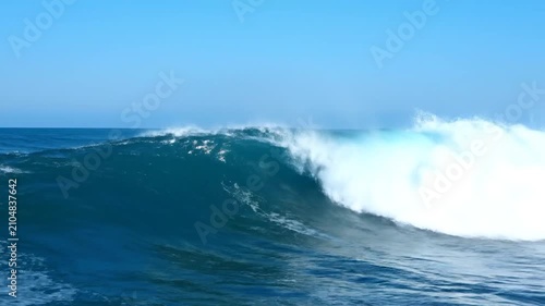 A powerful blue ocean wave curls under a clear summer sky
