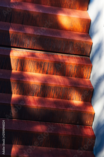 Bild auf Leinwand Dappled sunlight on ridged rusty metal facade