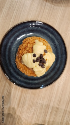 Top view of a dessert plate with sweet pastry, whipped cream, and chocolate chips on a wooden table