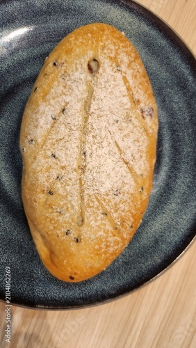 Top view of a fresh baked sourdough loaf on a black plate over a wooden surface