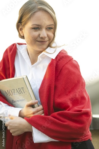 Self-confidently looking young woman, pianist, in white blouse and red cardigan, in the evening light, holding notes with Mozart, piano sonatas, in her arms, Stuttgart, Baden-Württemberg, Germany