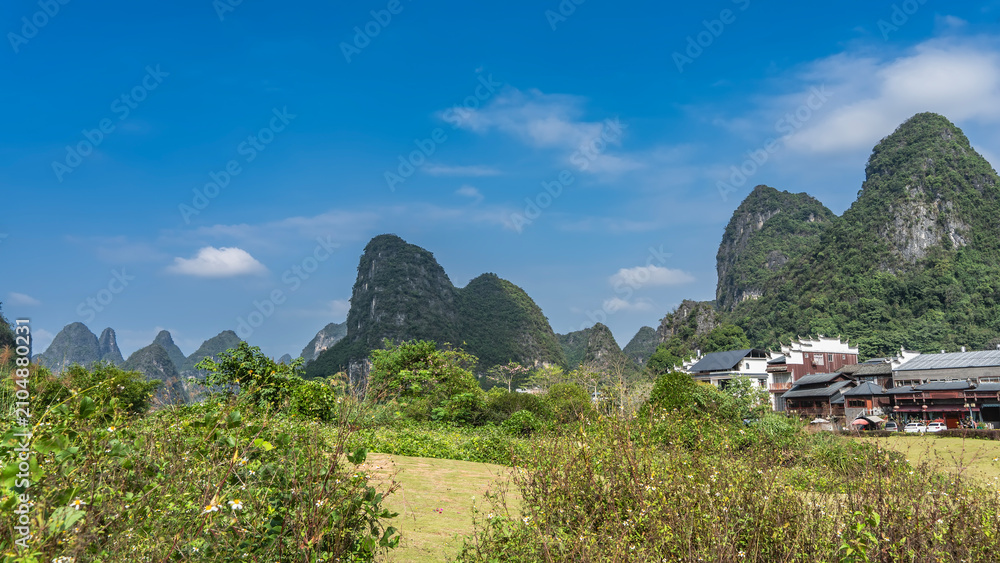 Obraz premium Picturesque mountain landscape. High hills with rounded peaks and green vegetation on the slopes. In the foreground there is a meadow, grass, bushes. China. Yangshuo.