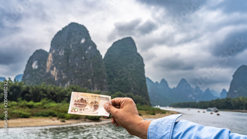 A 20 yuan banknote in a man's hand. The background is a picturesque mountain and river depicted on the money. China. Li River. Li Jiang. Guilin