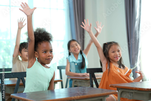 Multiethnic children raising hands to answer question in classroom