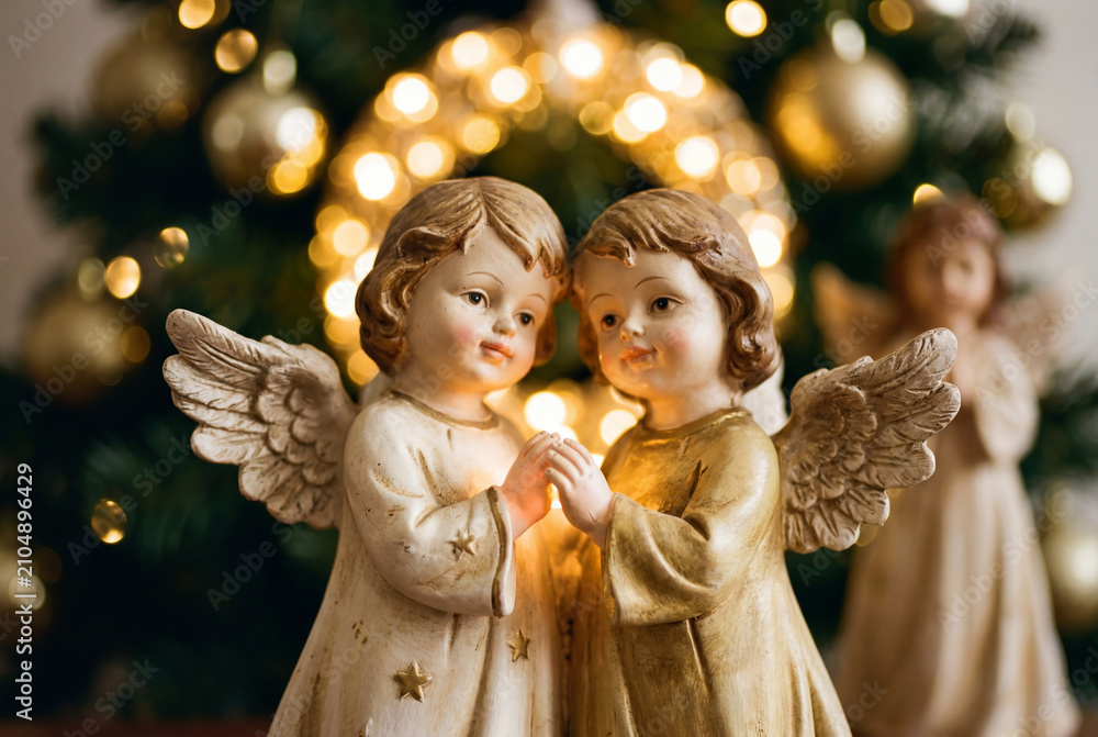 Fototapeta premium Two cute vintage christmas angel figurines near lit tree
