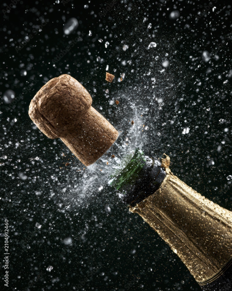 Obraz premium Cork from champagne bottle pops with mist and particles flying in a dark setting captured in studio. Dynamic moment of celebration is shown.