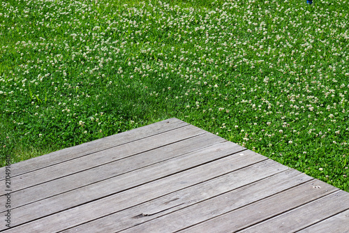 Photos Wooden deck edge with light brown planks adjacent to lush green grass and white