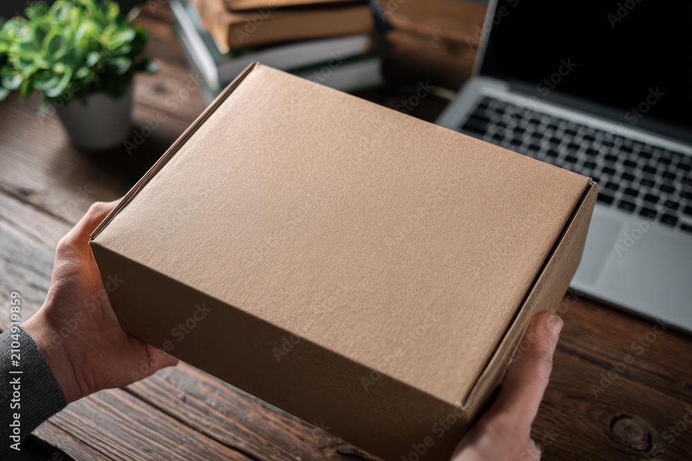 Fototapeta premium Hands holding a cardboard box on a wooden desk