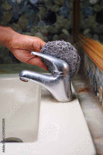 Photography Hand scrubbing a bathroom faucet with a cleaning sponge