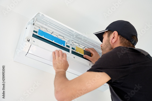 Man checking air conditioner filter in an open wall mounted split unit during maintenance. Concept of HVAC service, appliance care and seasonal cleaning