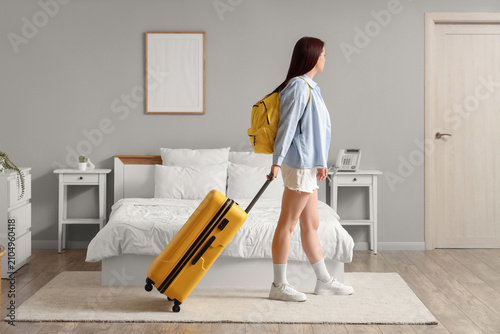 Young woman with a yellow suitcase and backpack walking through a modern hotel room  ready for travel and adventure