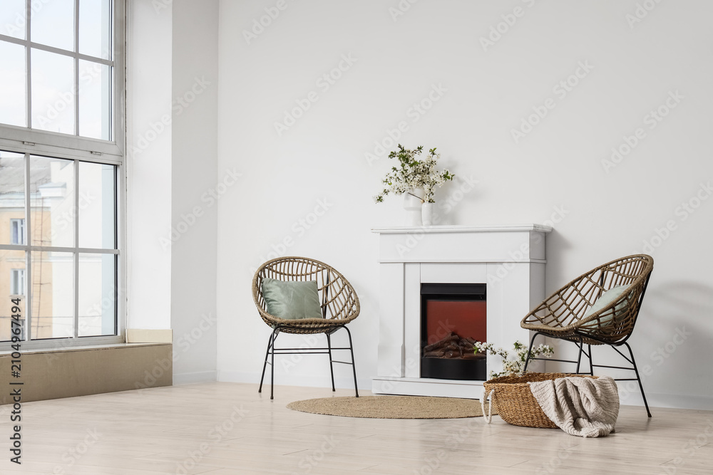 Obraz premium Interior of light living room with blooming branches in vases, fireplace and armchairs
