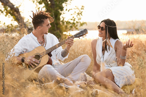 Schilderij op canvas Young couple of hippies with dreadlocks playing guitar outdoors