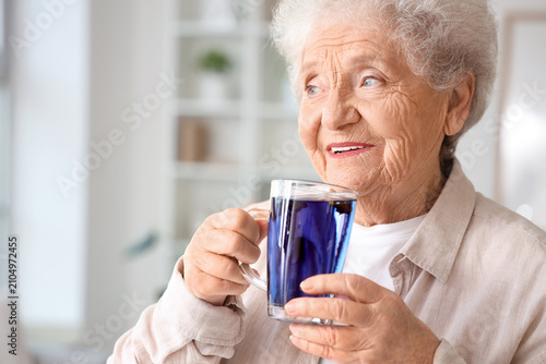 Foto Senior woman with glass cup of butterfly pea flower tea in living room