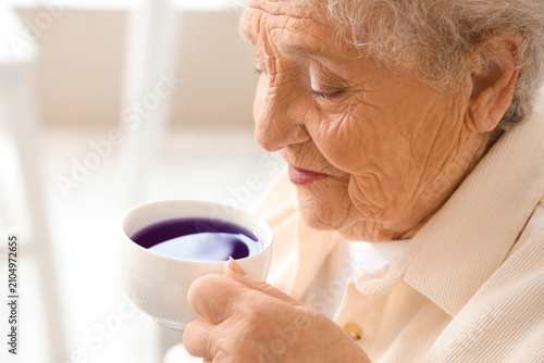 Cuadro en lienzo Senior woman with cup of butterfly pea flower tea at home, closeup