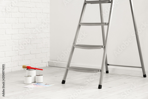 Foto Stepladder with cans of paint and brush near white wall