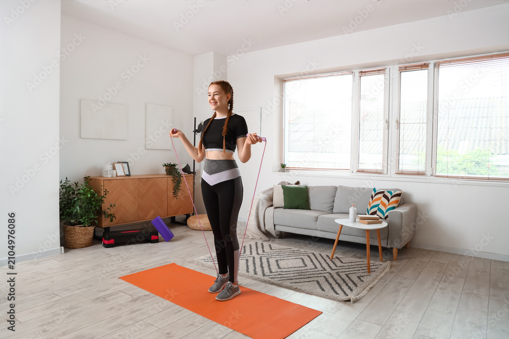 Fototapeta premium Sporty young woman jumping with rope at home