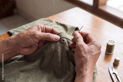 Elderly person sewing hole in green textile