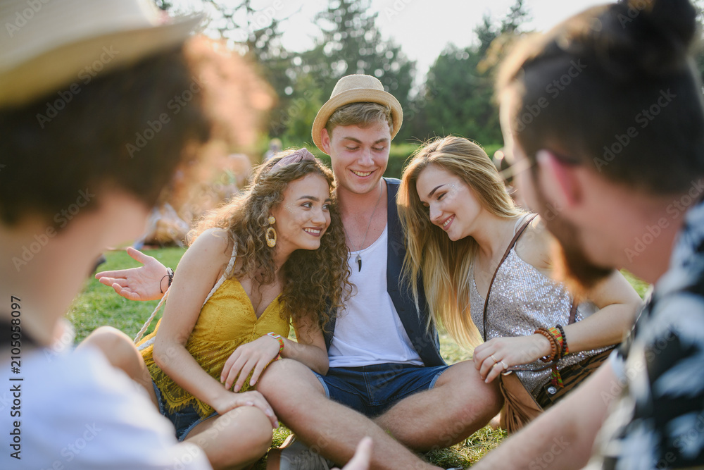 Fototapeta premium Group of young friends sitting on ground at summer festival.