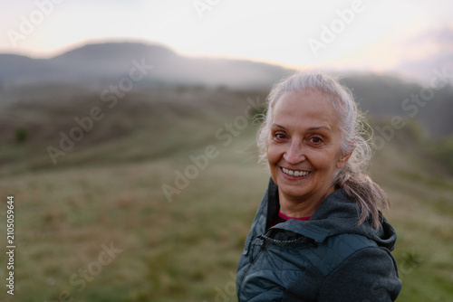 Senior woman hiking in nature on early morning with fog and mountains in background.
