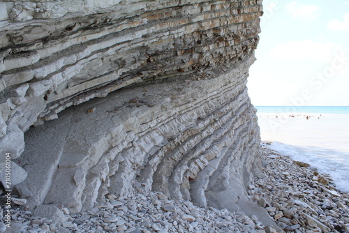 Fotografía Layered rock formation along the beach with ocean in background