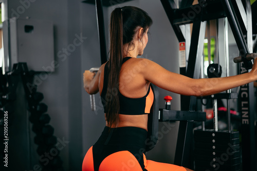 A woman is working out at a gym using a strength training machine. She is wearing athletic clothing and appears focused on her fitness routine