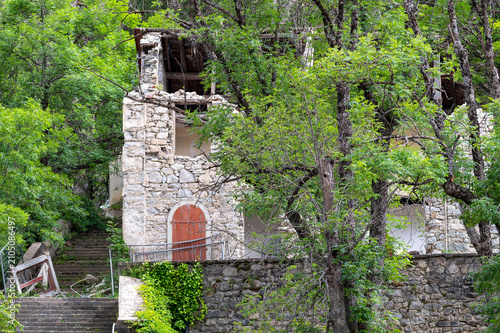 Canvas Print Old abandoned stone house in ruins with collapsed wooden roof structure on a wooded hillside, derelict rural building decaying in natural forest surroundings